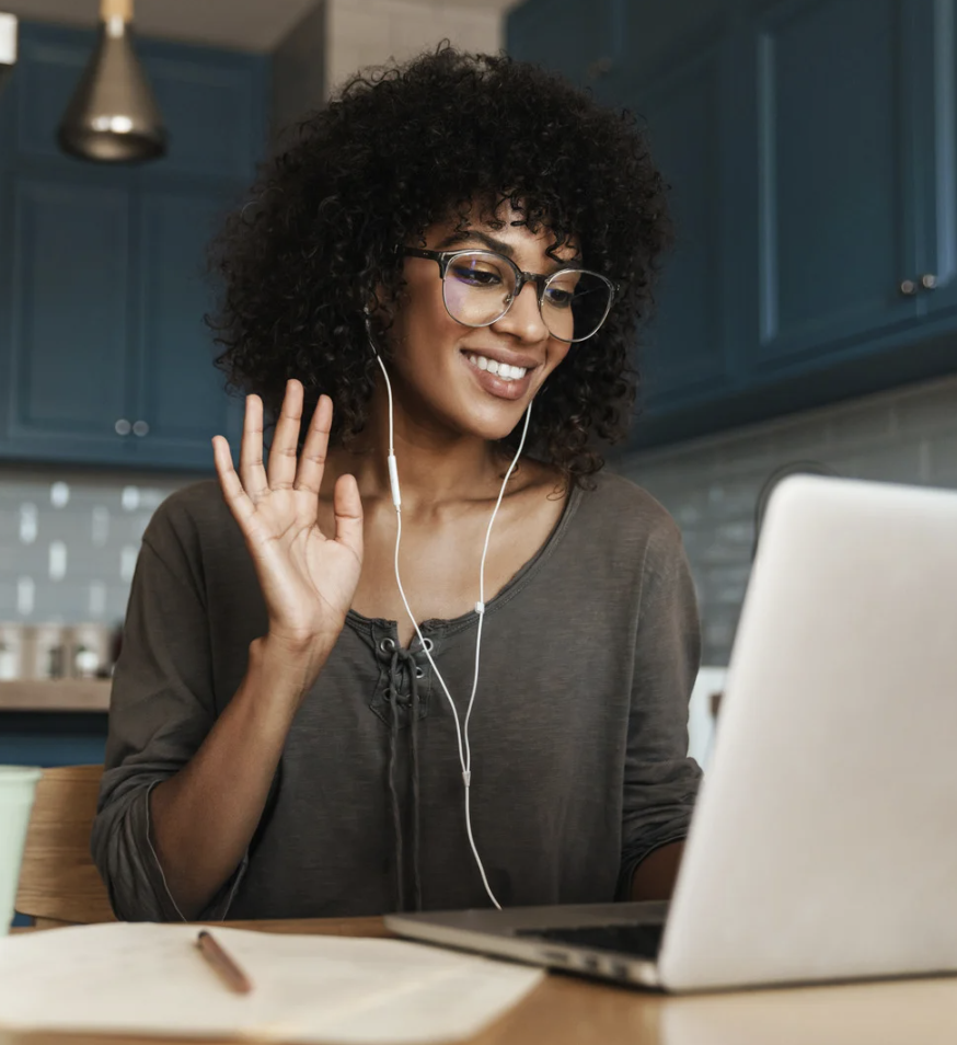 A brunette woman with a tan t-shirt and brown pants enjoys time outside. She is facing the camera in a relaxed pose, smili...